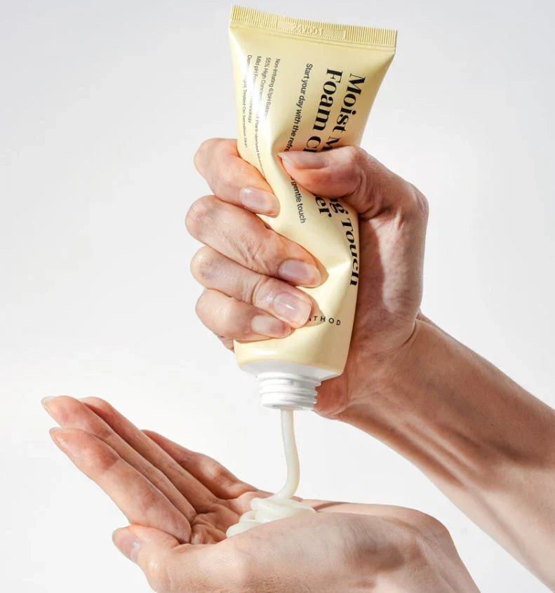 Hand squeezing a tube of cream onto another hand against a white background